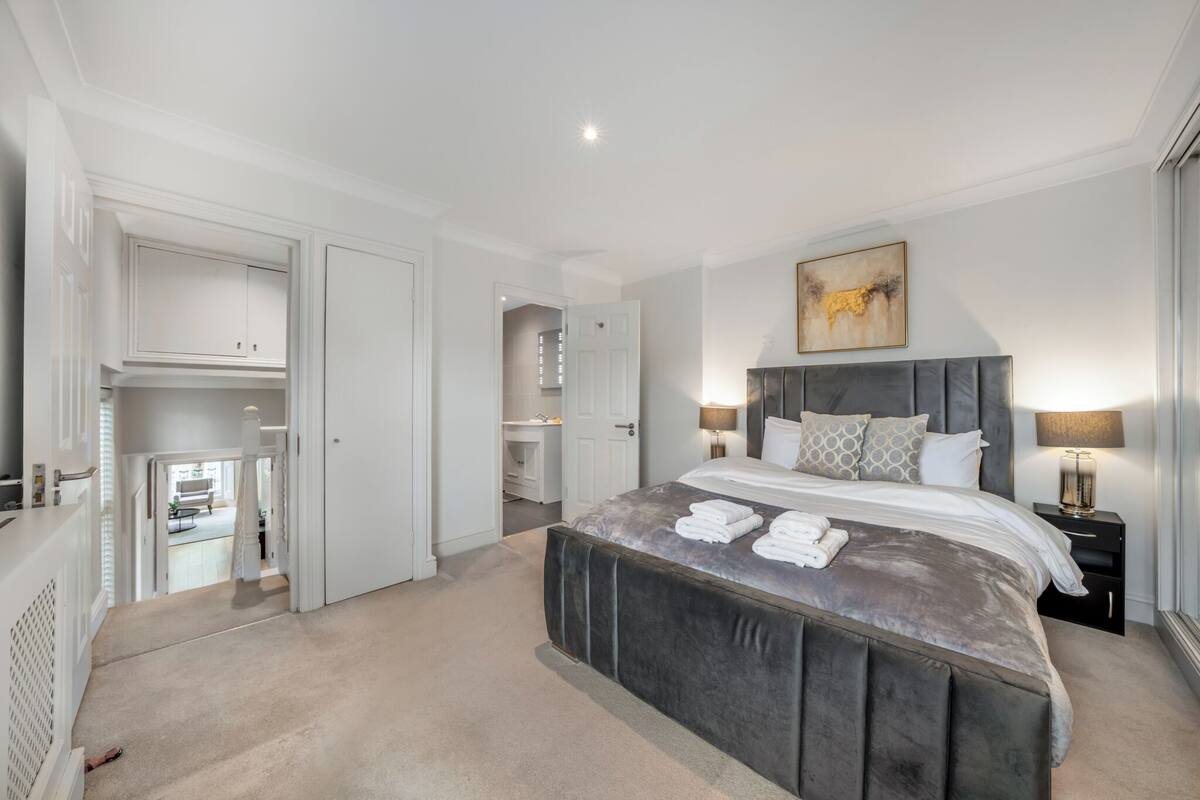 A bedroom with a large bed, bedside lamps, a headboard, and a painting on the wall.