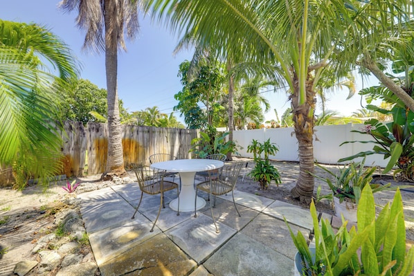 A patio with a round table and chairs, surrounded by palm trees and potted plants.
