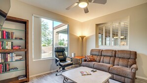 A living room with a sofa, a coffee table, a bookshelf, a chair, and a window with blinds. - Golf Getaway! Surprise Gem w/ Covered Patio (Surprise)