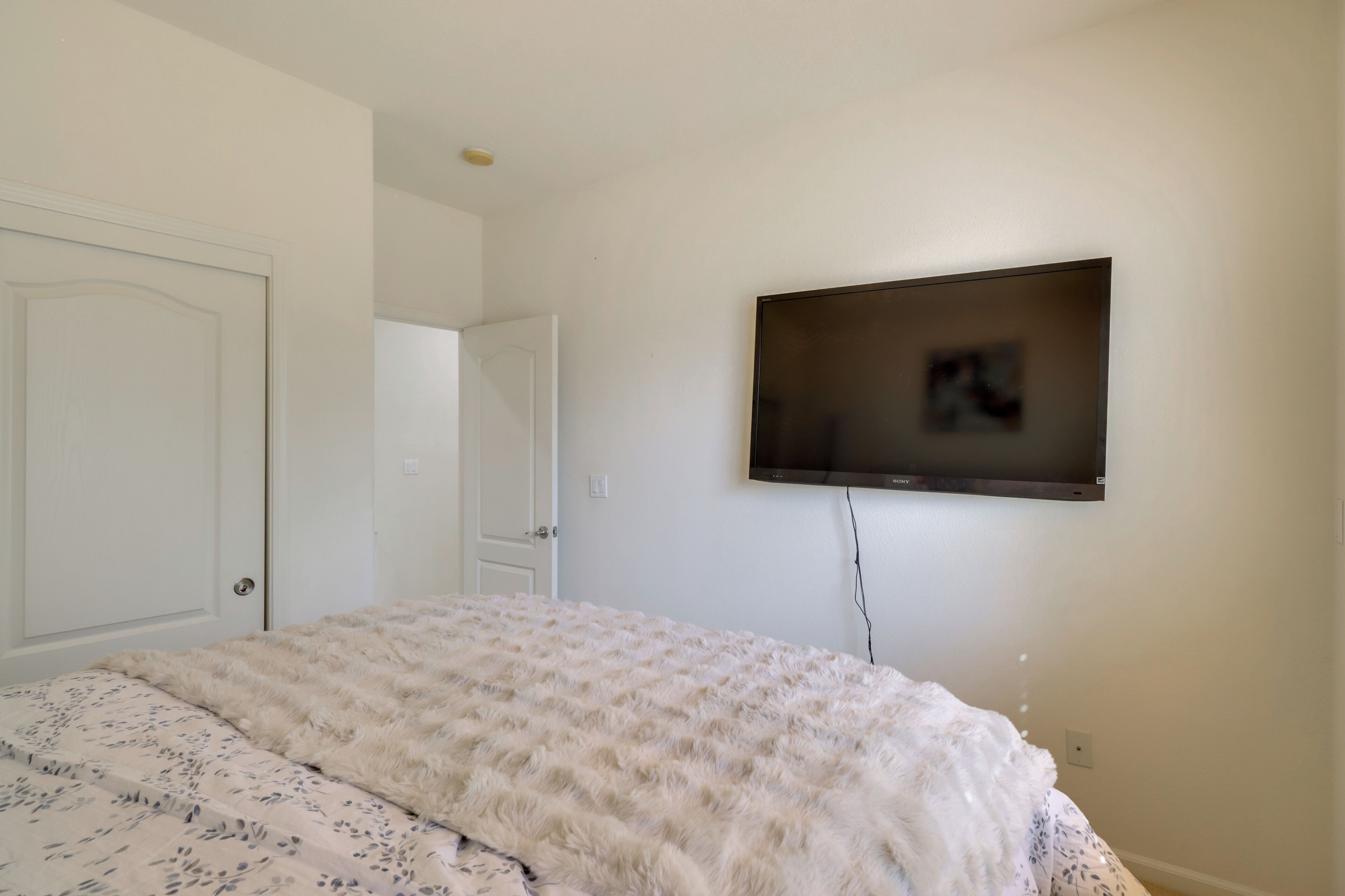 A bedroom with a bed, a television mounted on the wall, and a door.