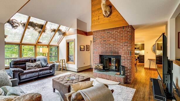 A spacious living room with a fireplace, a leather sofa, and a large window overlooking a deck. - 6 Mi to Okemo! Family Townhome in Lakeside Resort (Plymouth)