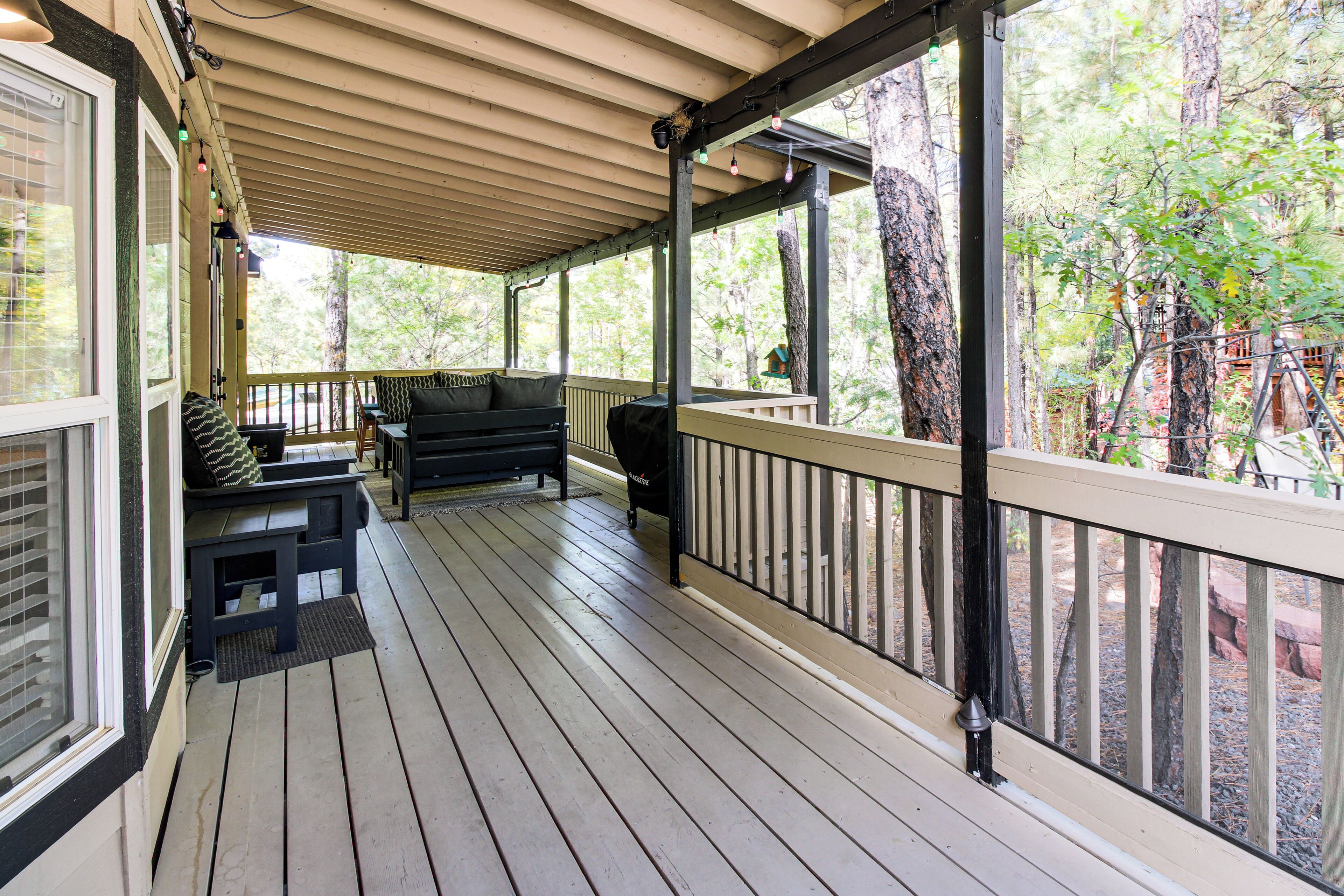 A covered porch with wooden flooring, a black sofa, and a grill.
