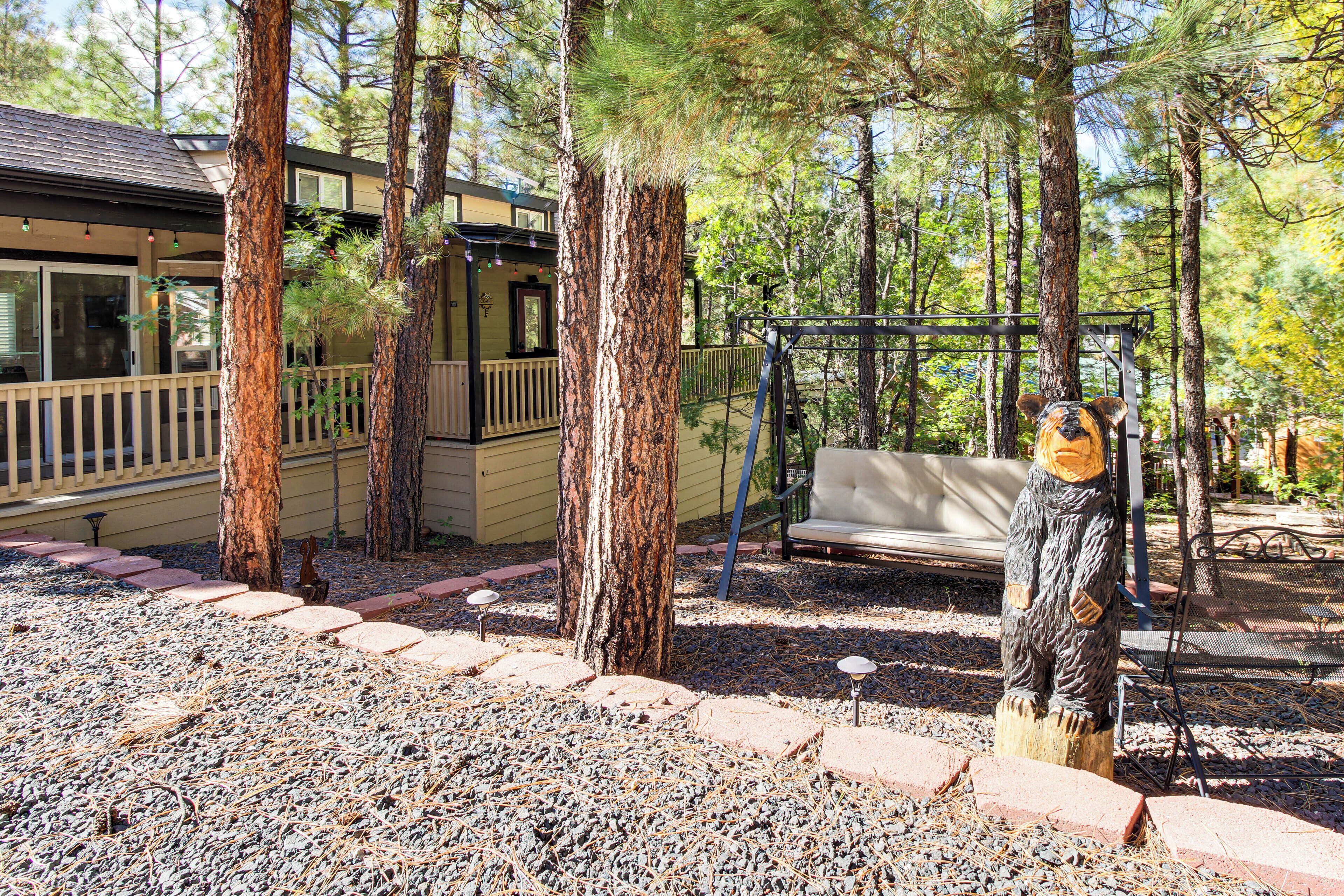 A wooden cabin with a deck, surrounded by trees and a swing set.