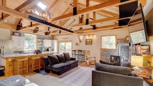A spacious living area with a high ceiling, wooden beams, a fireplace, and a kitchen with bar stools. - 7 Mi to Bilger's Rocks: Secluded 7-acre Retreat (Curwensville)