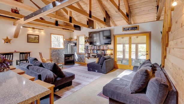 A cozy living room with wooden beams, a fireplace, a TV, and comfortable seating. - 7 Mi to Bilger's Rocks: Secluded 7-acre Retreat (Curwensville)