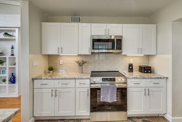 A modern kitchen with white cabinetry, a stainless steel microwave, a built-in oven, and a coffee maker.
