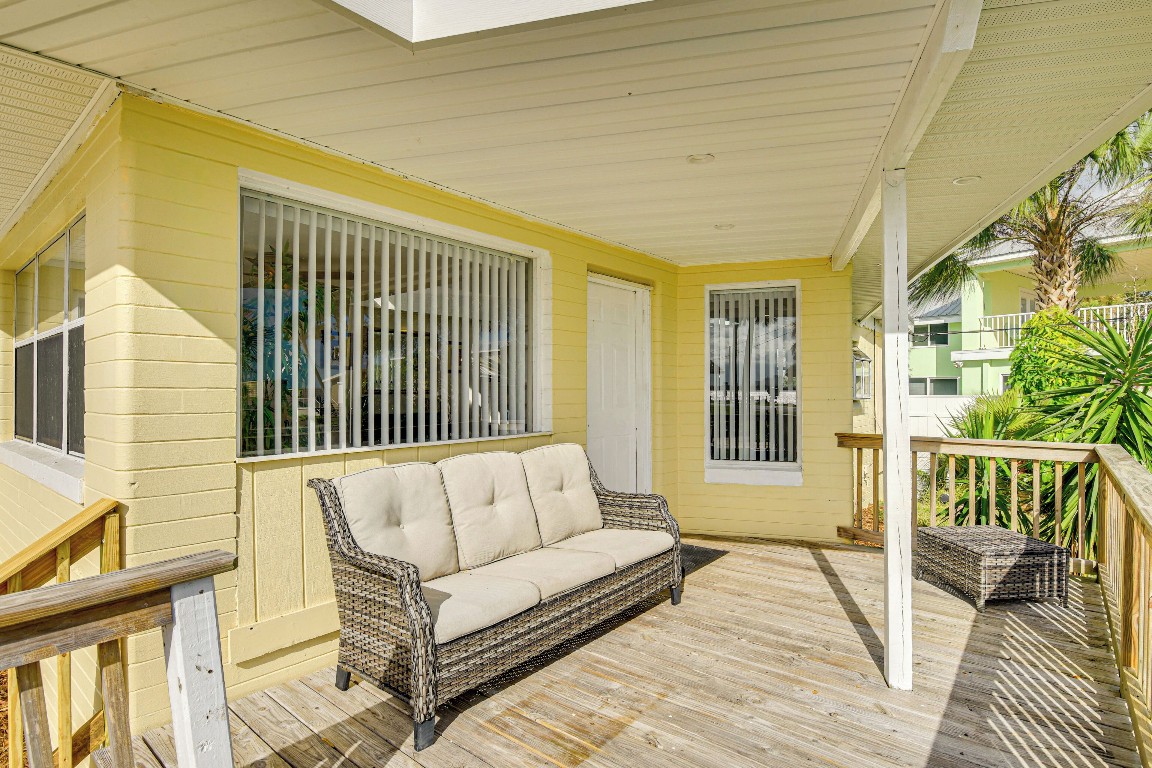 A covered outdoor area with a wicker sofa, wooden deck, and a railing.