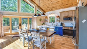 A spacious kitchen with wooden flooring, a dining area with white chairs, and a large window overlooking greenery. - Secluded Lake Lanier Cabin w/ Game Area (Gainesville)