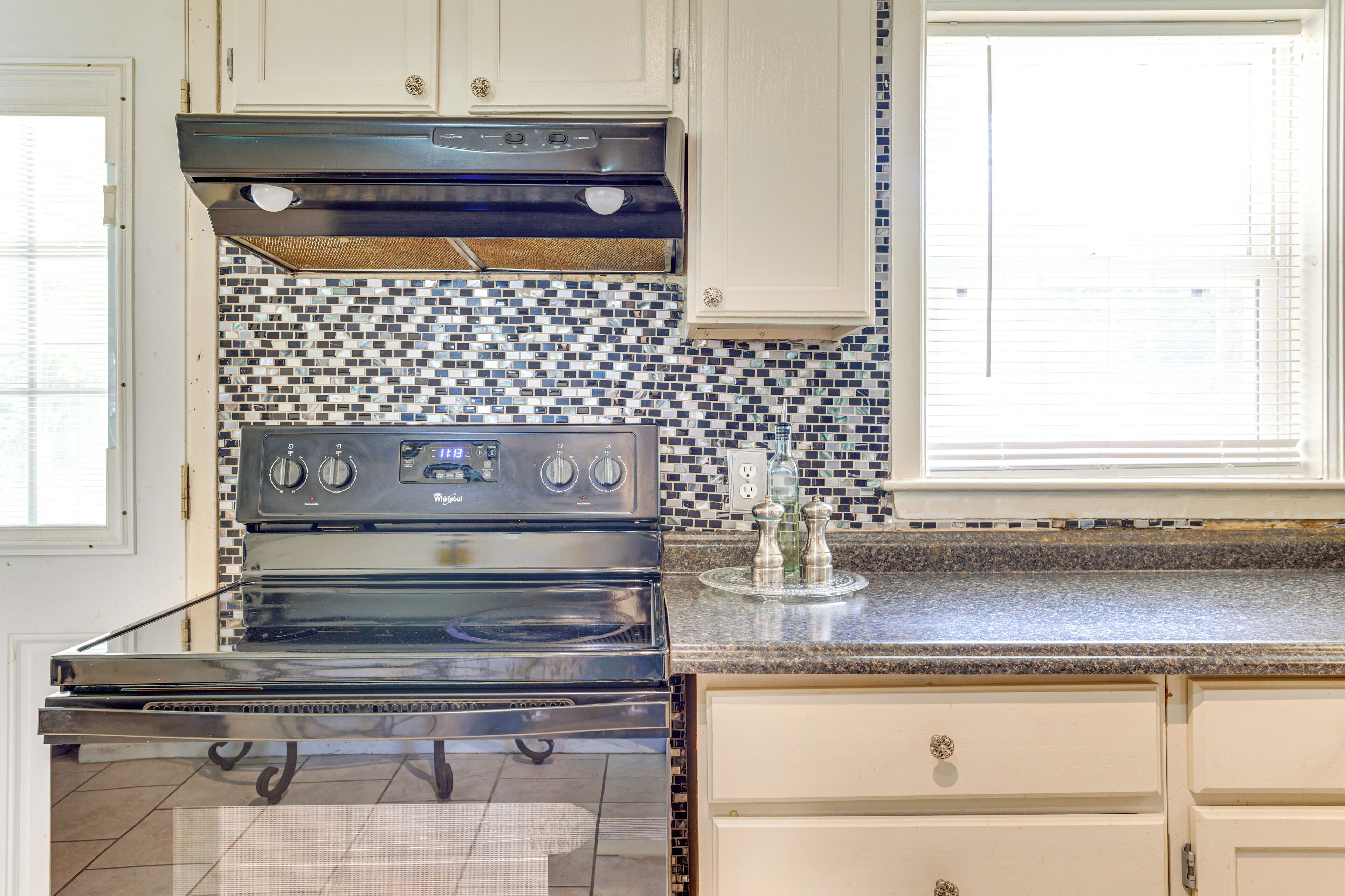 A kitchen with a black stove, white cabinets, and a blue and white tiled backsplash.