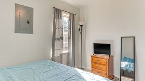 Une chambre à coucher comprenant un lit, une commode, un téléviseur, un miroir et une fenêtre avec des rideaux.