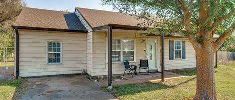 A single-story house with a covered porch, a small patio, and a tree in front.