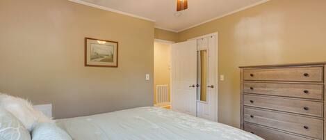 A bedroom with a bed, a dresser, a ceiling fan, and a door leading to another room.