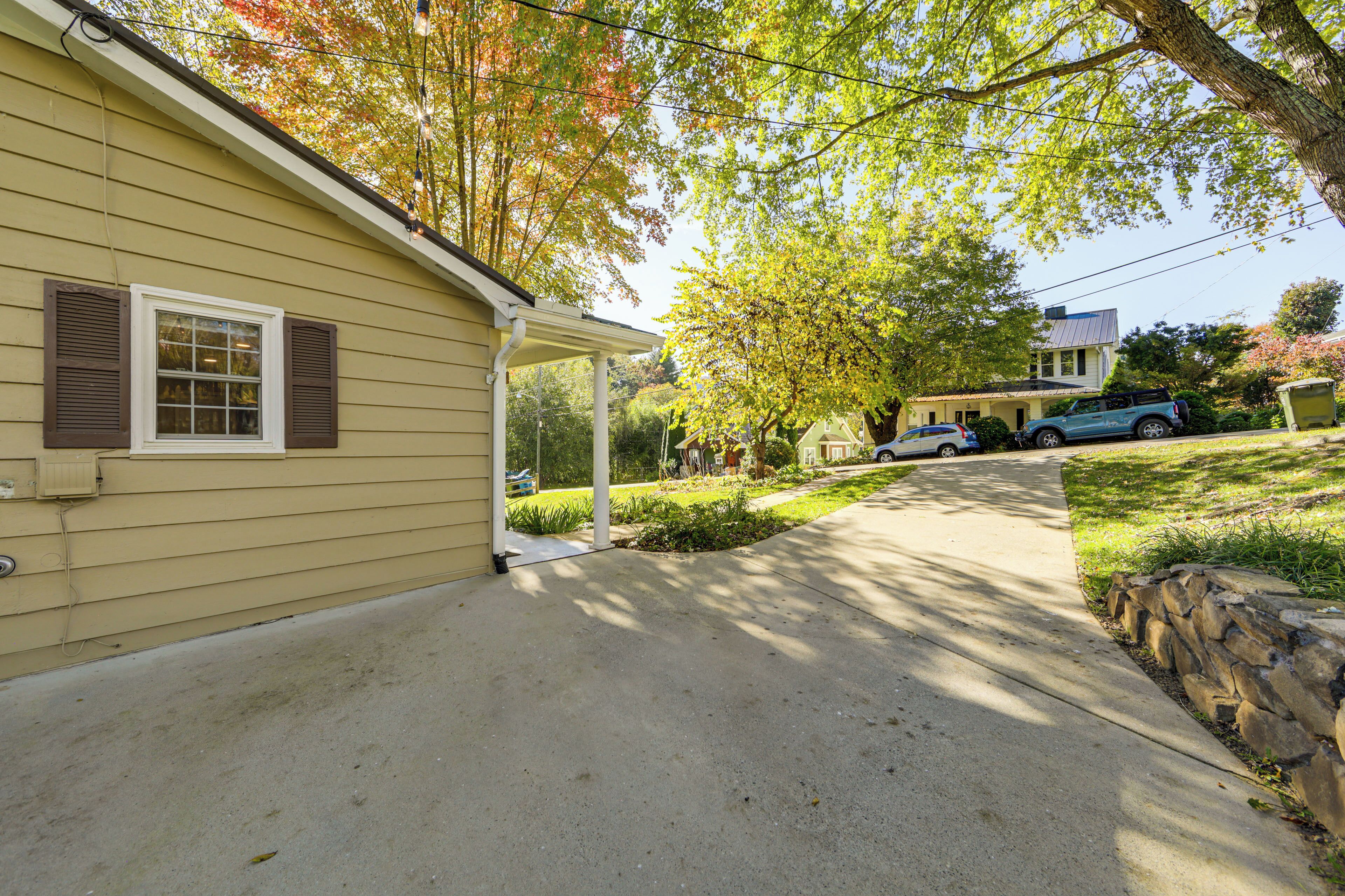 A residential driveway leading to a house with a covered porch, a stone retaining wall, and a parked car.