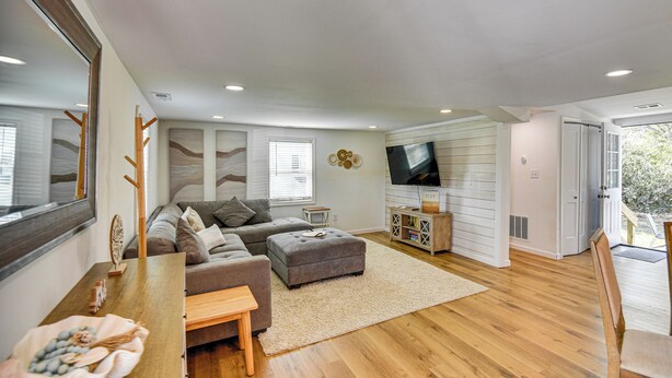 A modern living room with a sectional sofa, a wooden coffee table, a television, and a bookshelf. - Beach Days & Dtwn Charm! Cape Charles Cottage (Cape Charles)