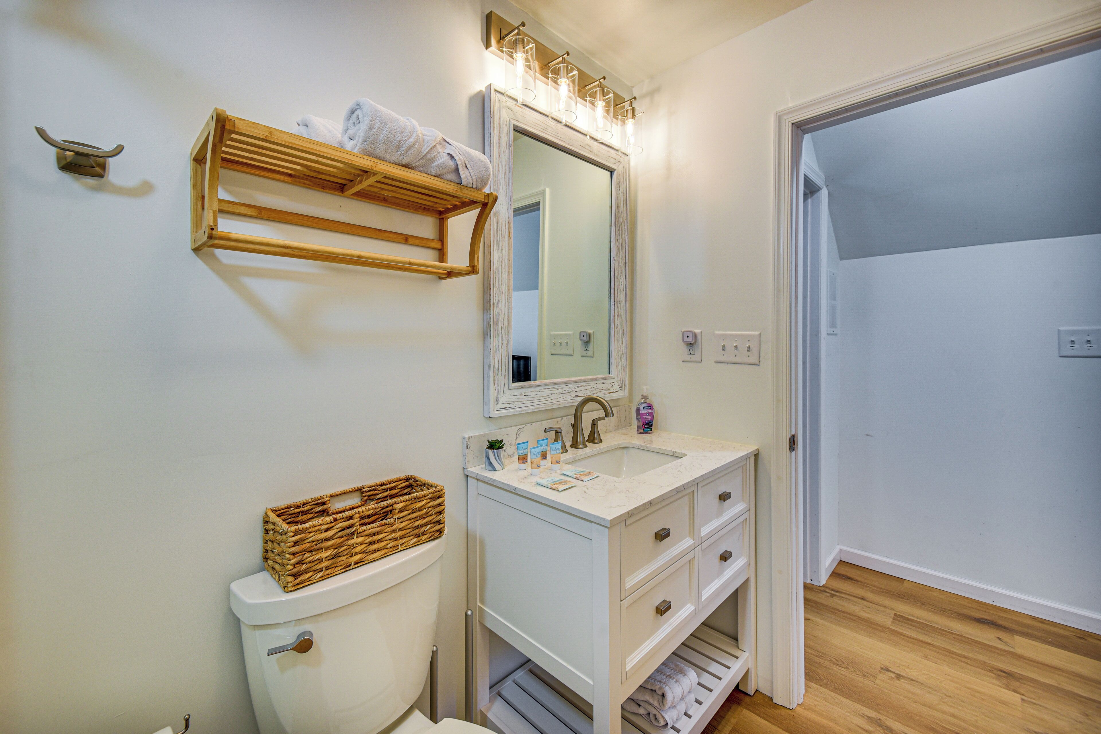 A bathroom with a toilet, sink, mirror, and wooden shelf.