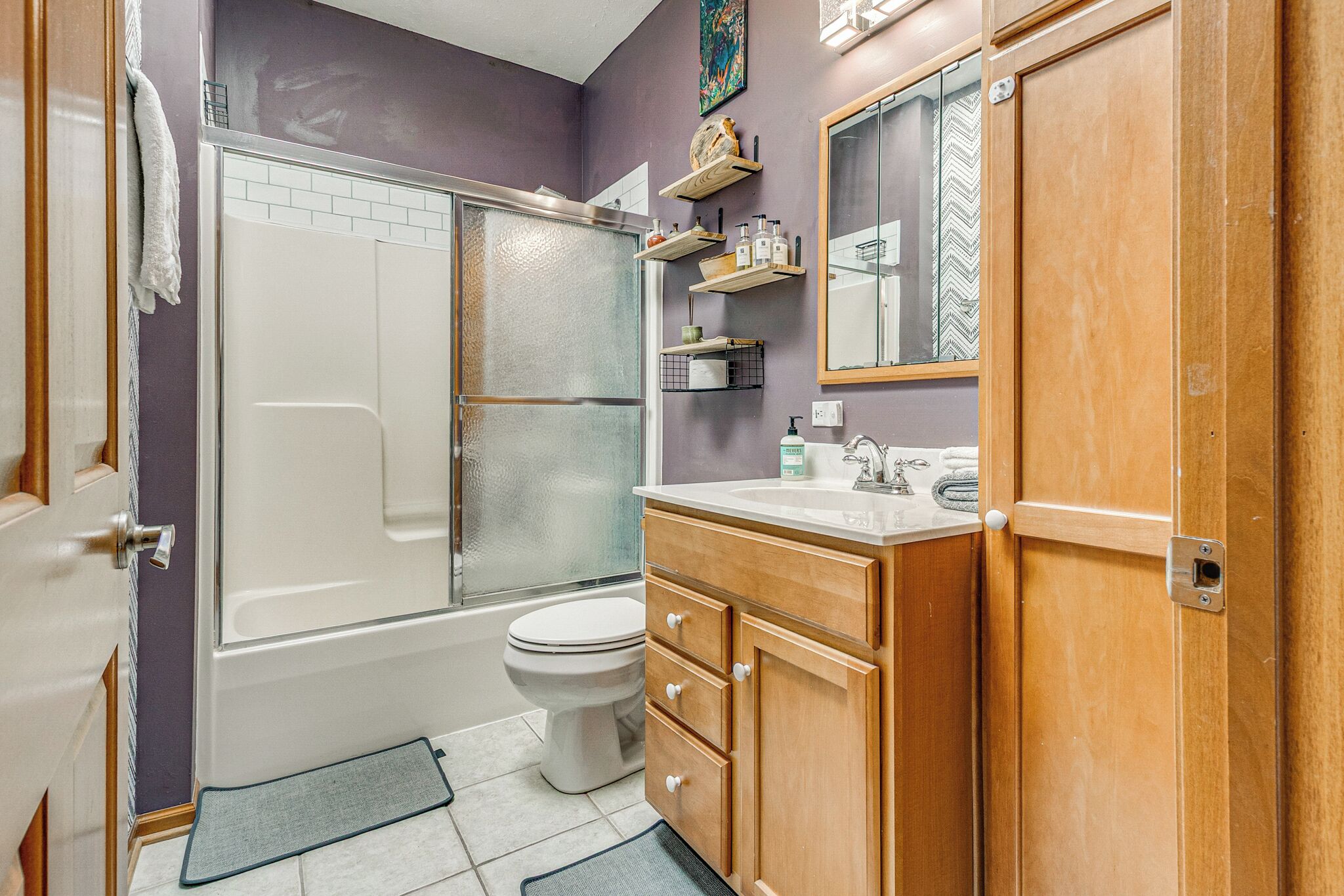 A bathroom with a shower, toilet, vanity, and shelves with toiletries.
