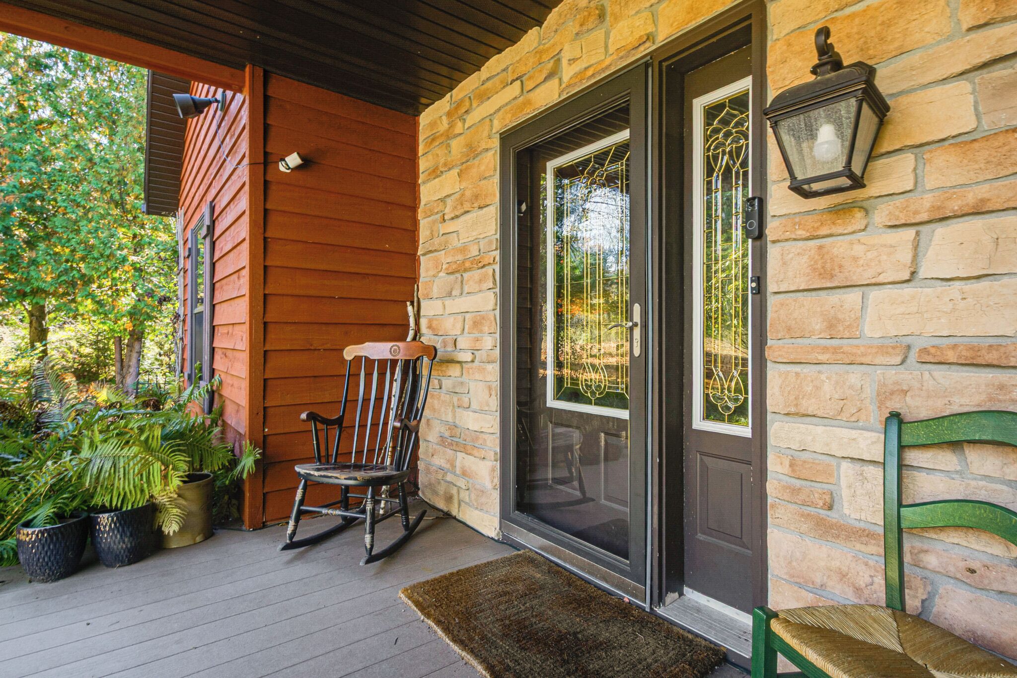 A wooden porch with a rocking chair, a bench, and potted plants.