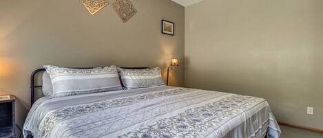 A bedroom with a large bed, a bedside table, and a wall-mounted lamp.