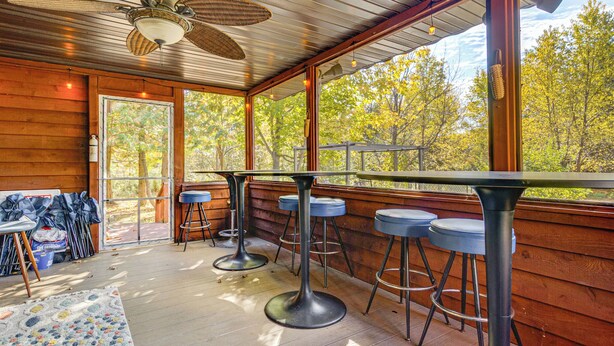 A wooden deck with a bar area, including stools and a table, and large windows offering a view of trees. - Stars & Sunsets! Door Peninsula Retreat w/ Deck (Egg Harbor)