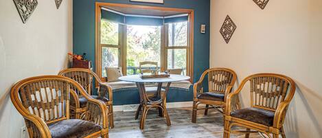 Huone, jossa on erkkeri-ikkuna, neljä rottinkituolia, pyöreä pöytä ja koristeellisia taideteoksia seinillä.