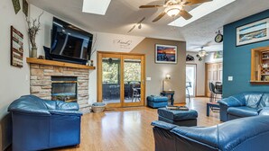 A spacious living room with a stone fireplace, leather sofas, a flat-screen TV, and a ceiling fan. - Stars & Sunsets! Door Peninsula Retreat w/ Deck (Egg Harbor)
