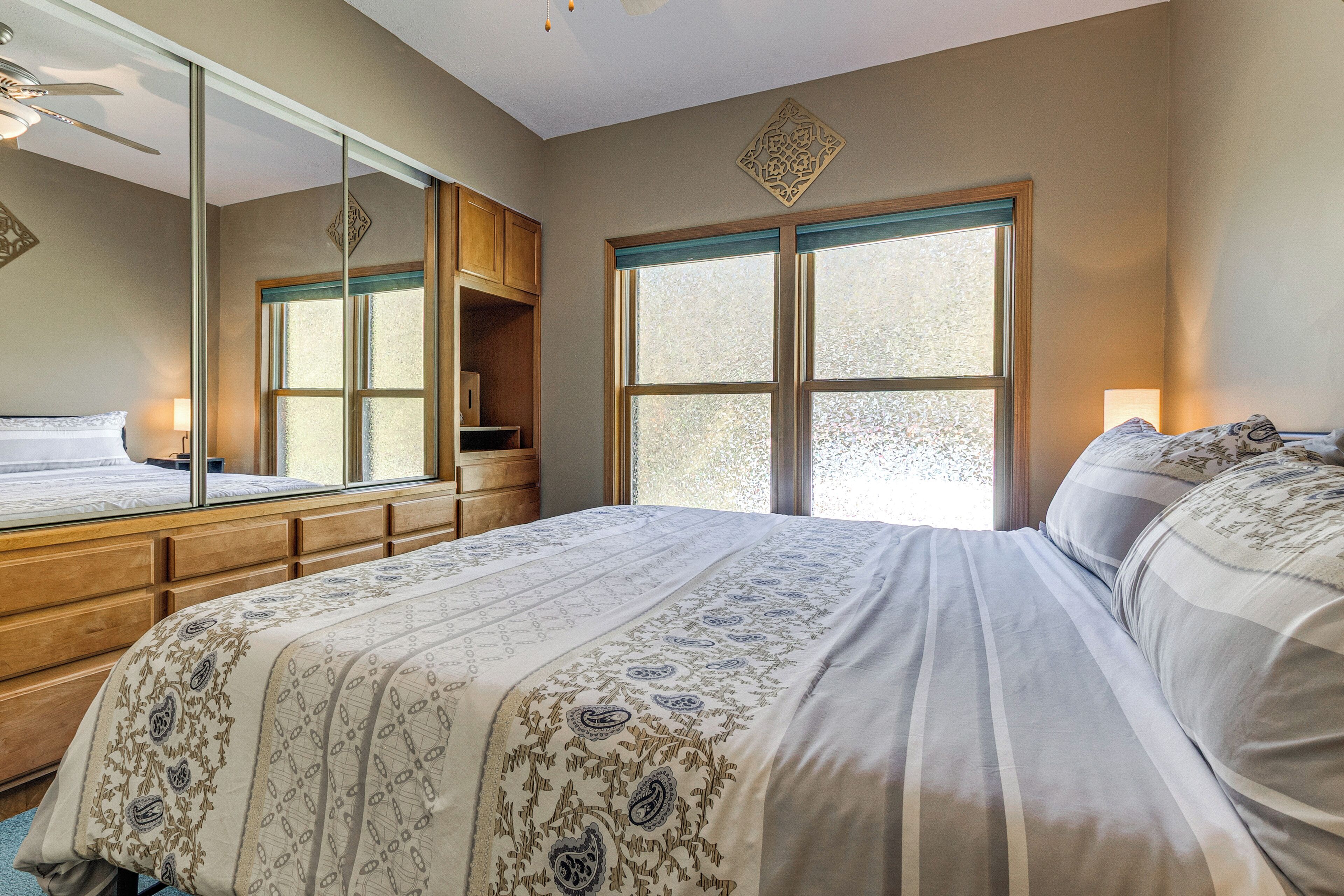 A bedroom with a large bed, a wooden dresser, a mirror, and a window with frosted glass.
