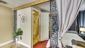 A hotel room with a bed, a bedside table, a potted plant, a door leading to a bathroom, and a decorative wall piece. - Convenient Studio w/ Private Bar in Odessa (Odessa)