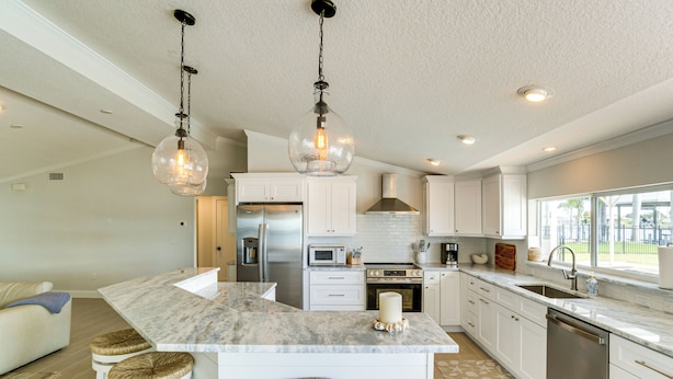 A modern kitchen with white cabinets, a marble island, stainless steel appliances, and hanging pendant lights.