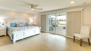 A bedroom with a bed, a chair, a ceiling fan, and a sliding glass door leading to an outdoor area.