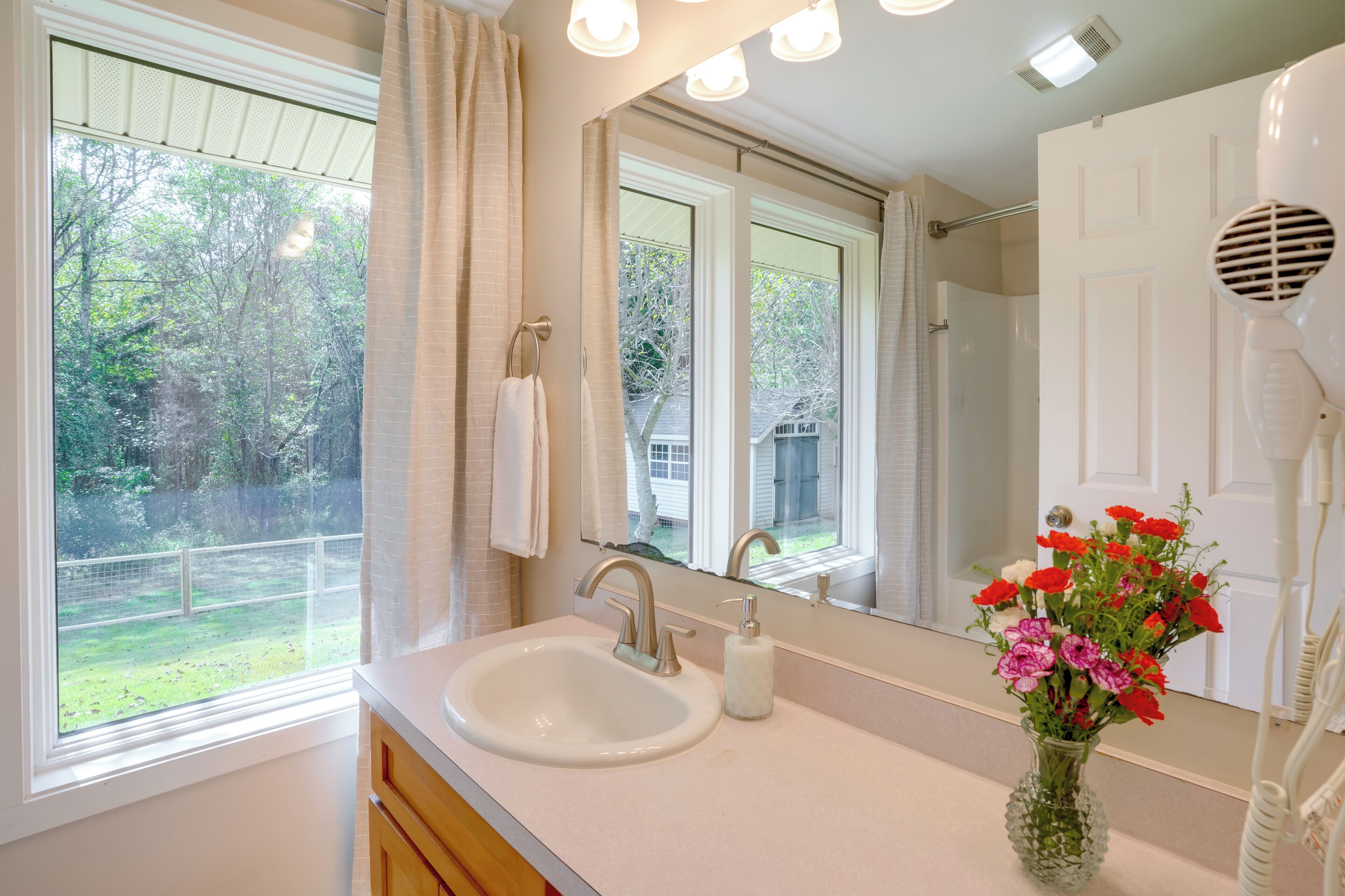 A bathroom with a sink, mirror, and a window with a view of a backyard.