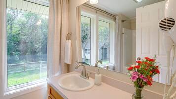 A bathroom with a sink, mirror, and a window with a view of a backyard.