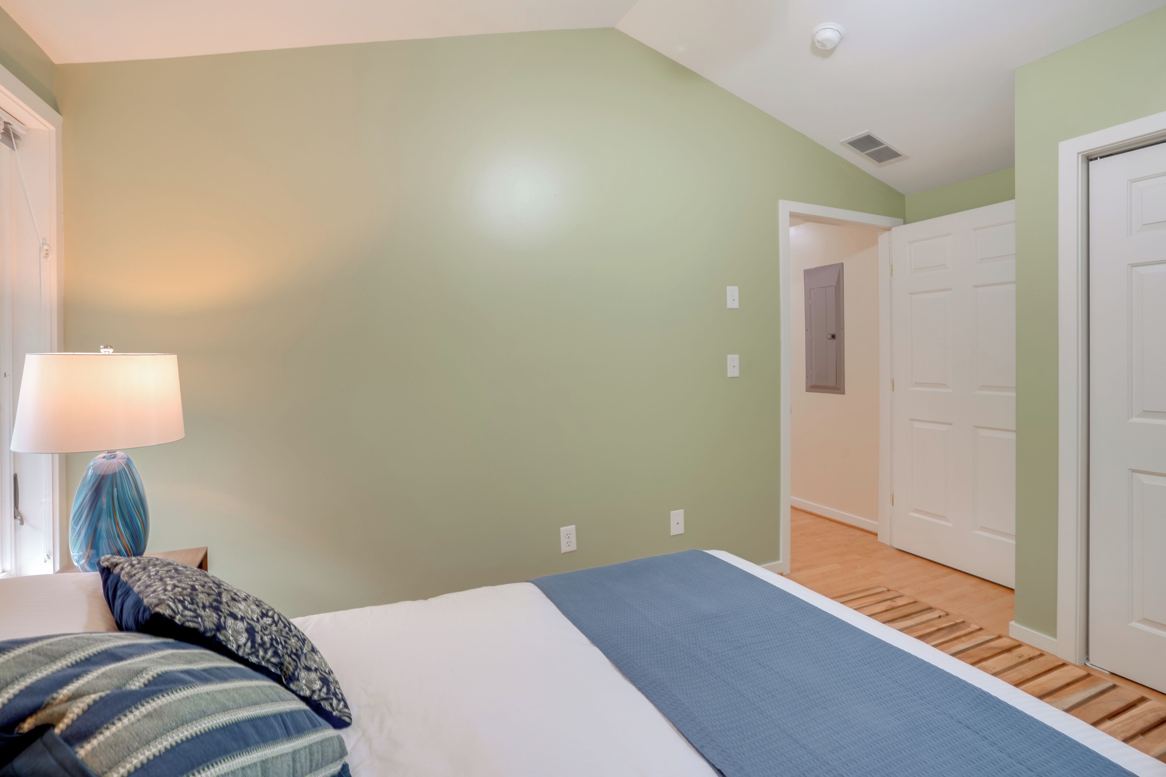 A bedroom with a bed, a lamp, and a door leading to another room.