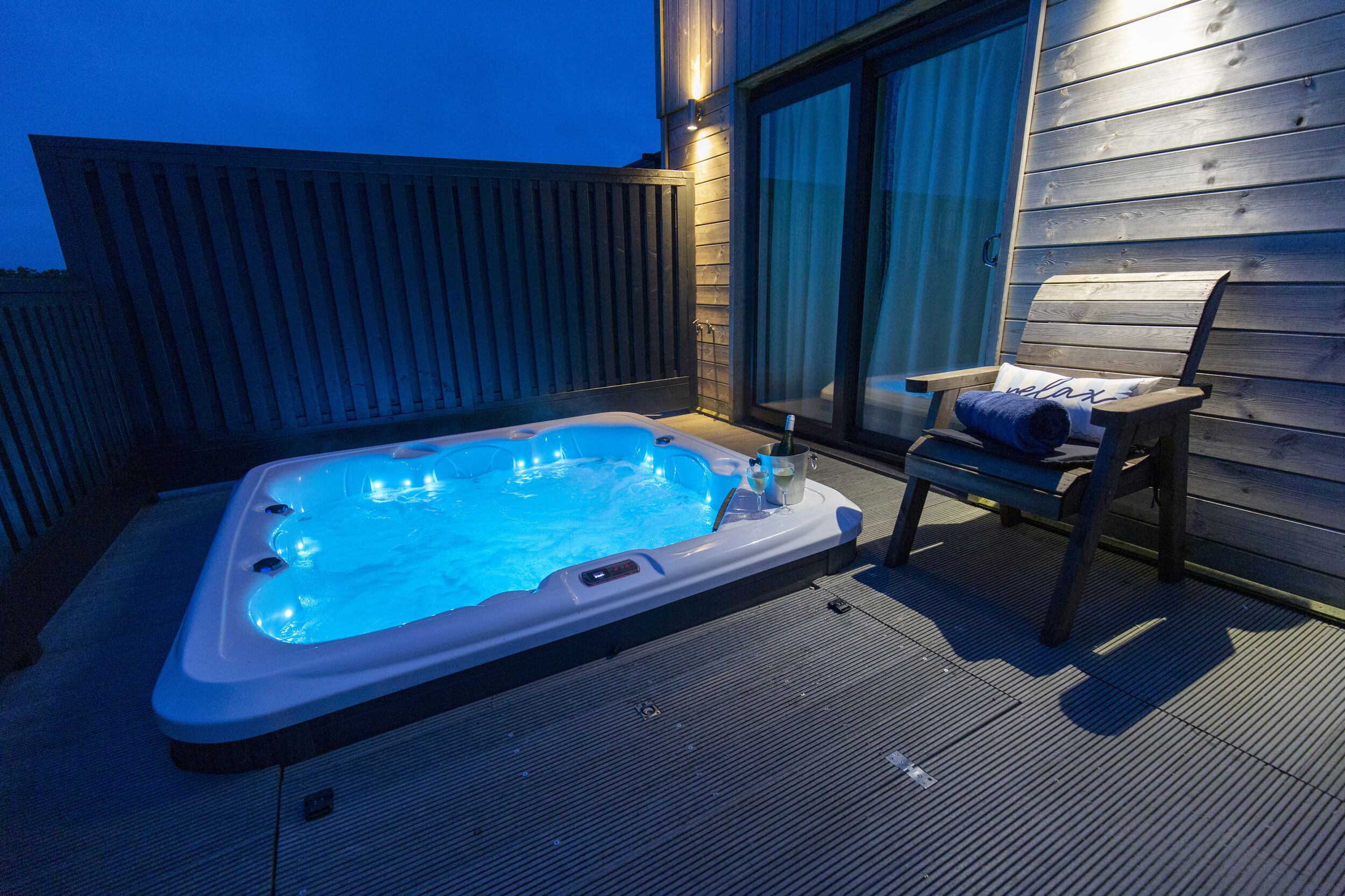 Un bain à remous sur une terrasse en bois, avec une chaise et une serviette.