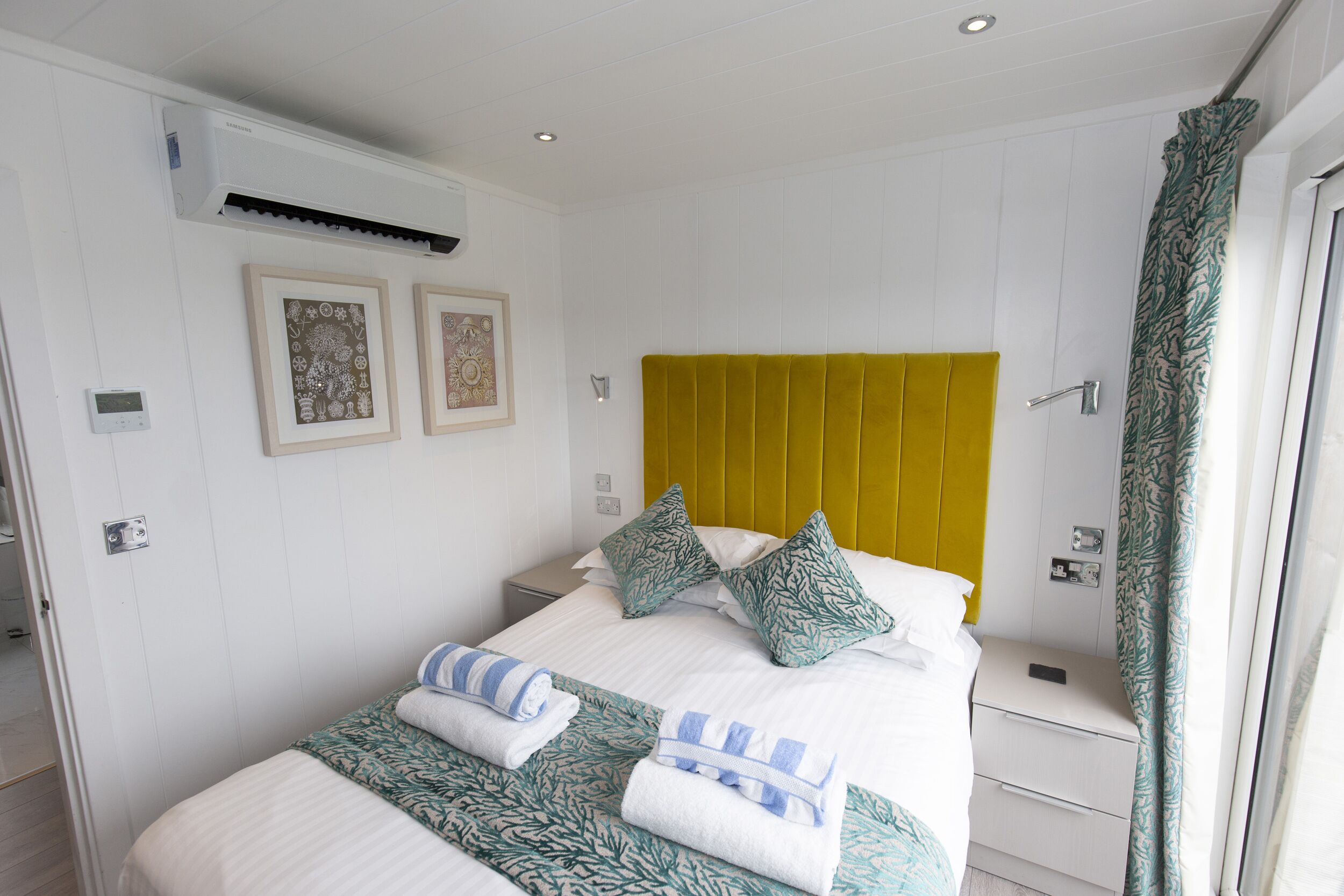 A neatly made bed with pillows, a bedside table, and a wall-mounted air conditioner.