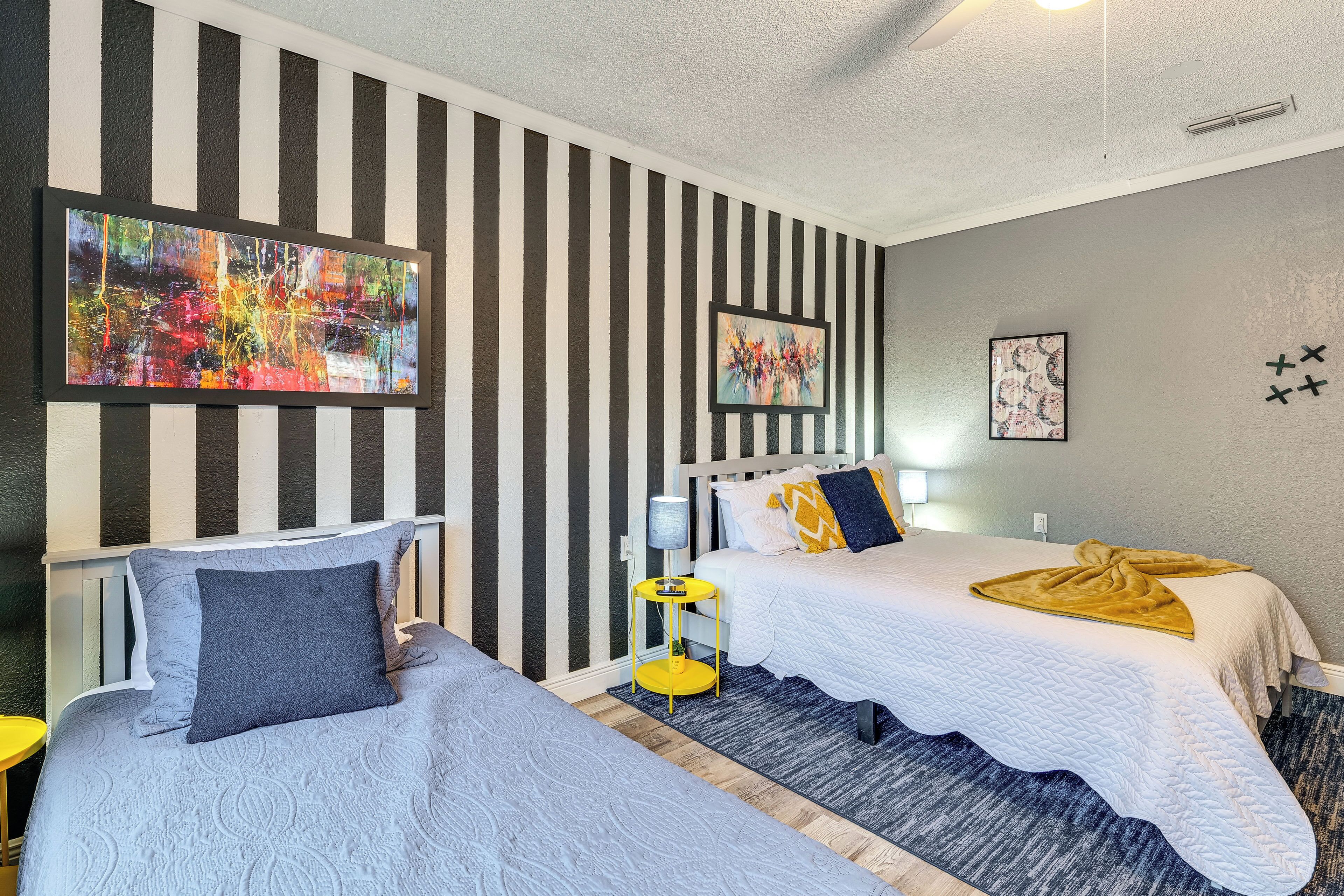 Una habitación de hotel con dos camas, paredes a rayas y obras de arte.
