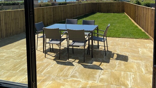 A patio with a table and chairs, a wooden fence, and a view of the sea and distant buildings. - Stunning Renovated Three Bedroom House (Poole)