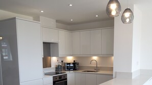 A modern kitchen with white cabinetry, a built-in oven, a microwave, and a kettle. - Stunning Renovated Three Bedroom House (Poole)