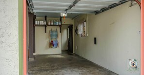 Un pasillo estrecho con piso de concreto, un marco de puerta metálico y un estante en la pared con productos de limpieza.