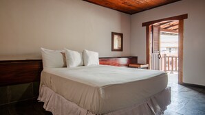 A bedroom with a wooden headboard, a bed with white bedding, a small table, and a balcony door. - Rede Andrade Galeão (Porto Seguro)