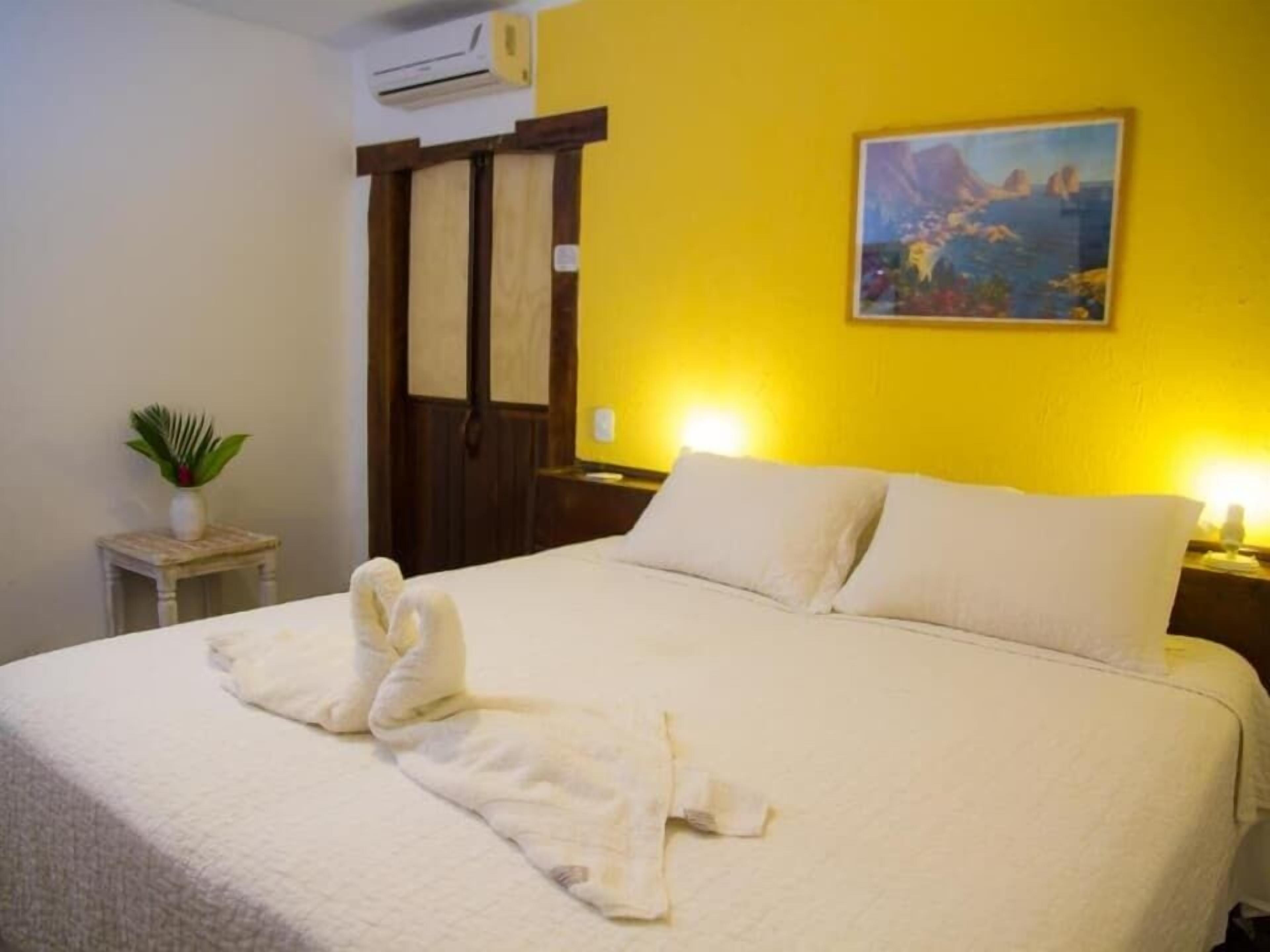 Una habitación de hotel con una cama, un cuadro en la pared y una planta sobre una mesita.