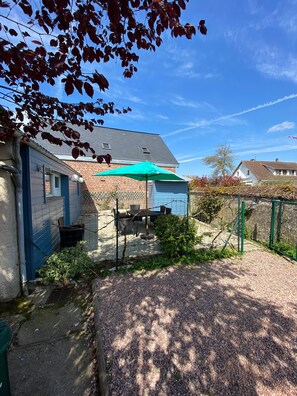 A residential property with a patio area, a brick house, and a green umbrella. - Apartment 'Le Jardin De Sasha Et La Noisette' with Private Terrace, Private Garden and Wi-Fi (Équemauville)