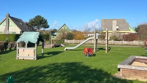 Une aire de jeux avec un toboggan, des structures d’escalade et une petite maison servant de cabane.