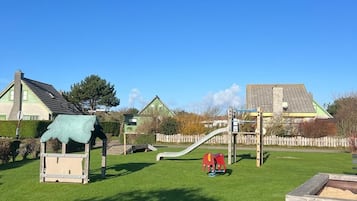 Une aire de jeux avec un toboggan, des structures d’escalade et une petite maison servant de cabane.