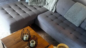 Un salon moderne avec un canapé gris, une table basse en bois et une table d’appoint en osier.