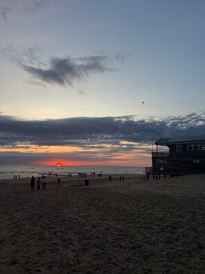 Ein Strand mit einem Rettungsschwimmturm und einem Sonnenuntergang im Hintergrund.