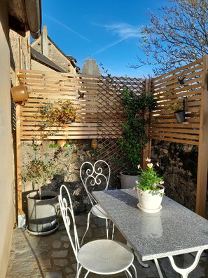 Un patio con una mesa y sillas, rodeado de plantas en macetas y una valla de madera.