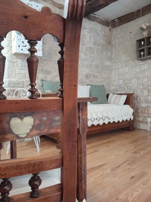Una cama de madera rústica con cubre lecho de encaje, una pared de piedra y una silla de madera con detalles tallados.