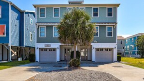 A multi-story residential building with a central entrance, two garages, and a palm tree in the front yard.