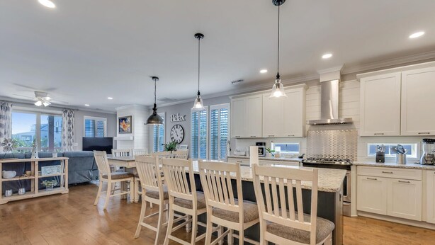 A modern kitchen with white cabinets, a dining area with wooden chairs, and a large window with a view.