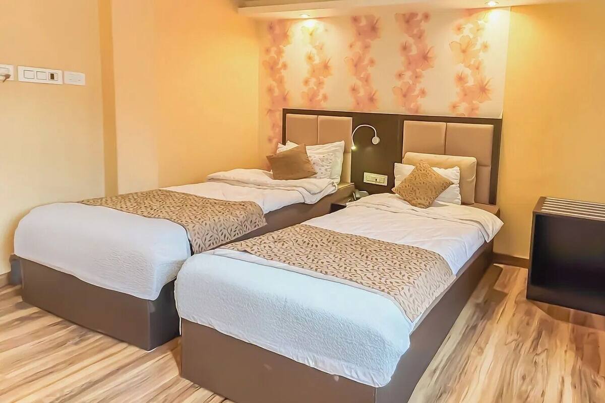 Een hotelkamer met twee bedden, een nachtkastje, een spiegel aan de muur en decoratief bloemenbehang.